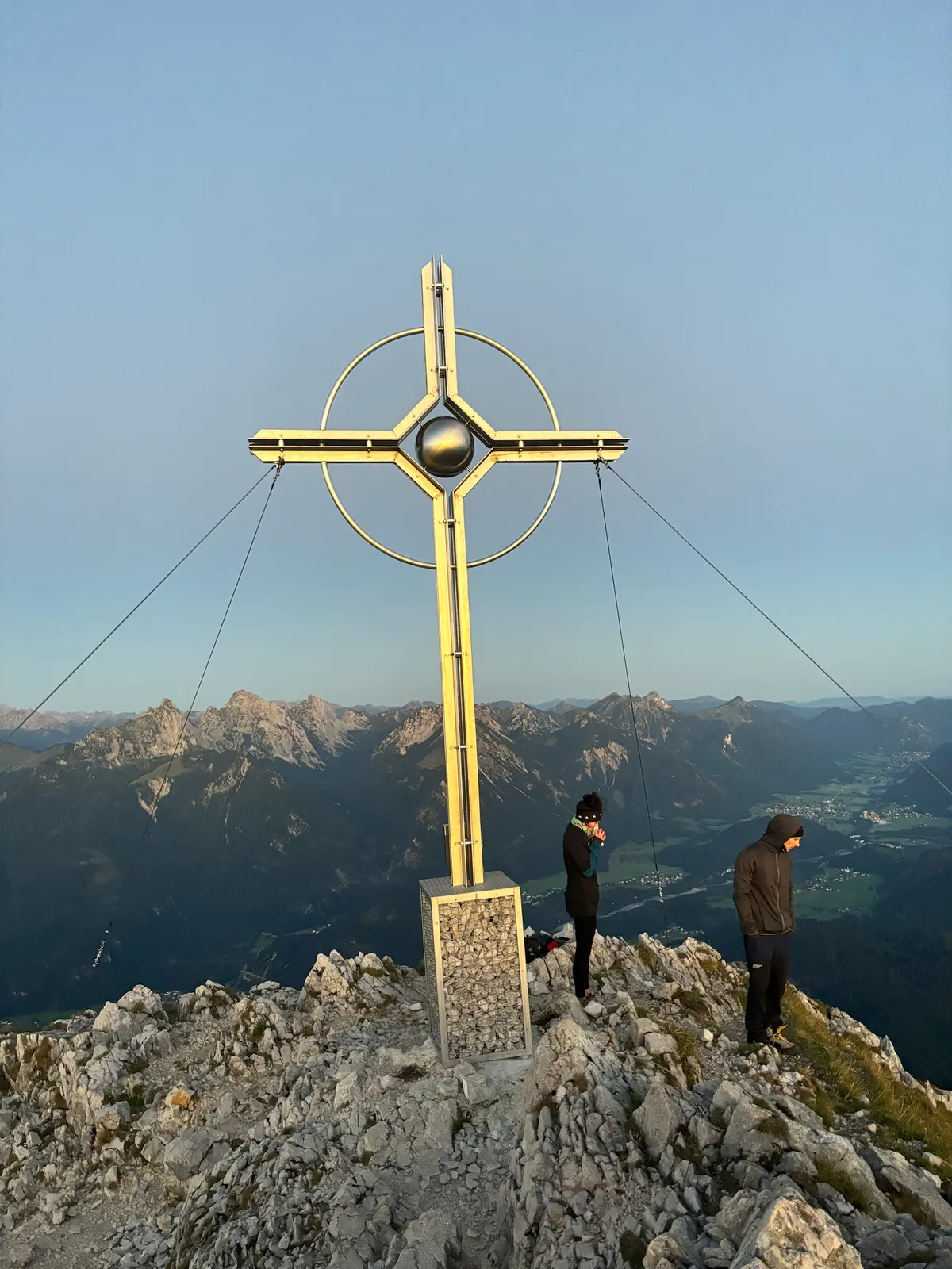 Zwei Leute am Gipfelkreuz im ersten Licht, Tannheimer Berge